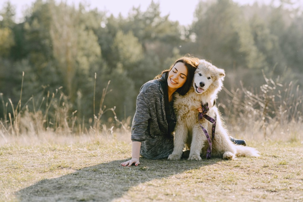 cheerful-woman-embracing-dog-while-sitting-on-grass-in-4148872